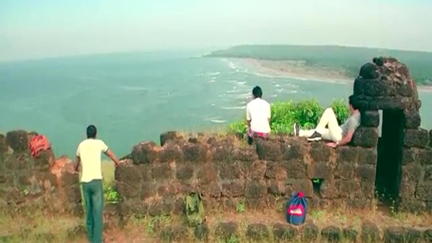 Three friends relaxing on ancient stone ruins overlooking a vast ocean coastline HD wallpaper