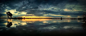 Dramatic Stormy Sunset Over Calm Lake With Silhouetted Trees And Cloud Reflections HD wallpaper