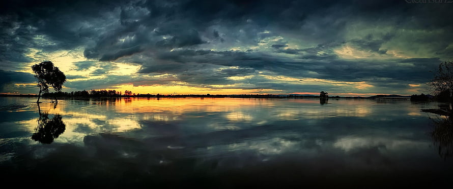 Dramatic Stormy Sunset Over Calm Lake With Silhouetted Trees And Cloud Reflections HD wallpaper