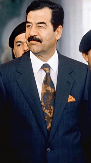 Saddam Hussein in a dark suit with patterned tie and pocket square HD phone wallpaper