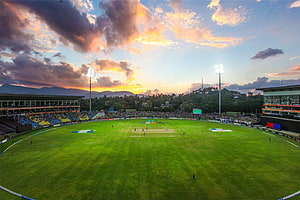 Vibrant Cricket Stadium at Sunset with Dramatic Clouds and Lush Green Pitch HD wallpaper