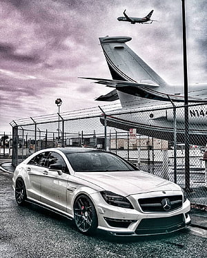 White Mercedes-Benz CLS 63 AMG parked near airport runway with airplane HD phone wallpaper