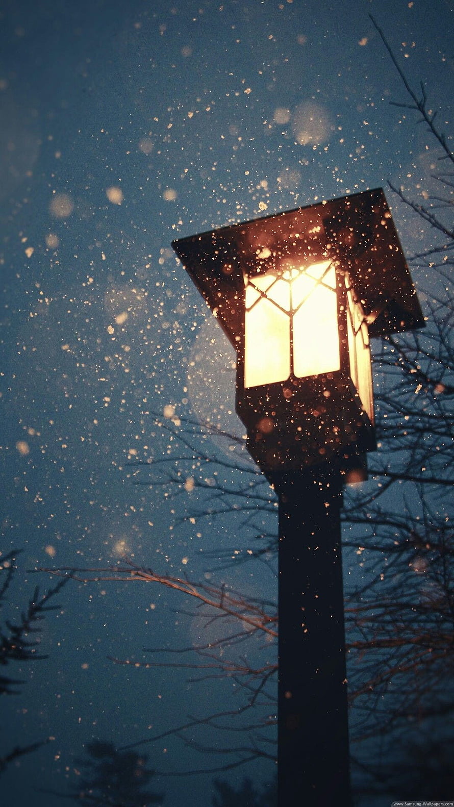 Glowing Street Lamp Illuminating Falling Snowflakes Against a Dark Blue Winter Sky HD phone wallpaper