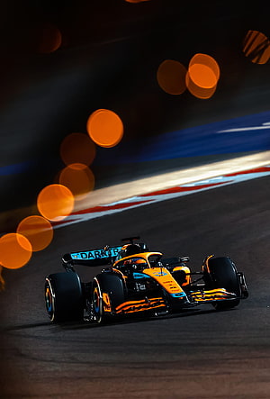 McLaren Formula 1 race car speeding on a night circuit with glowing orange bokeh lights HD phone wallpaper