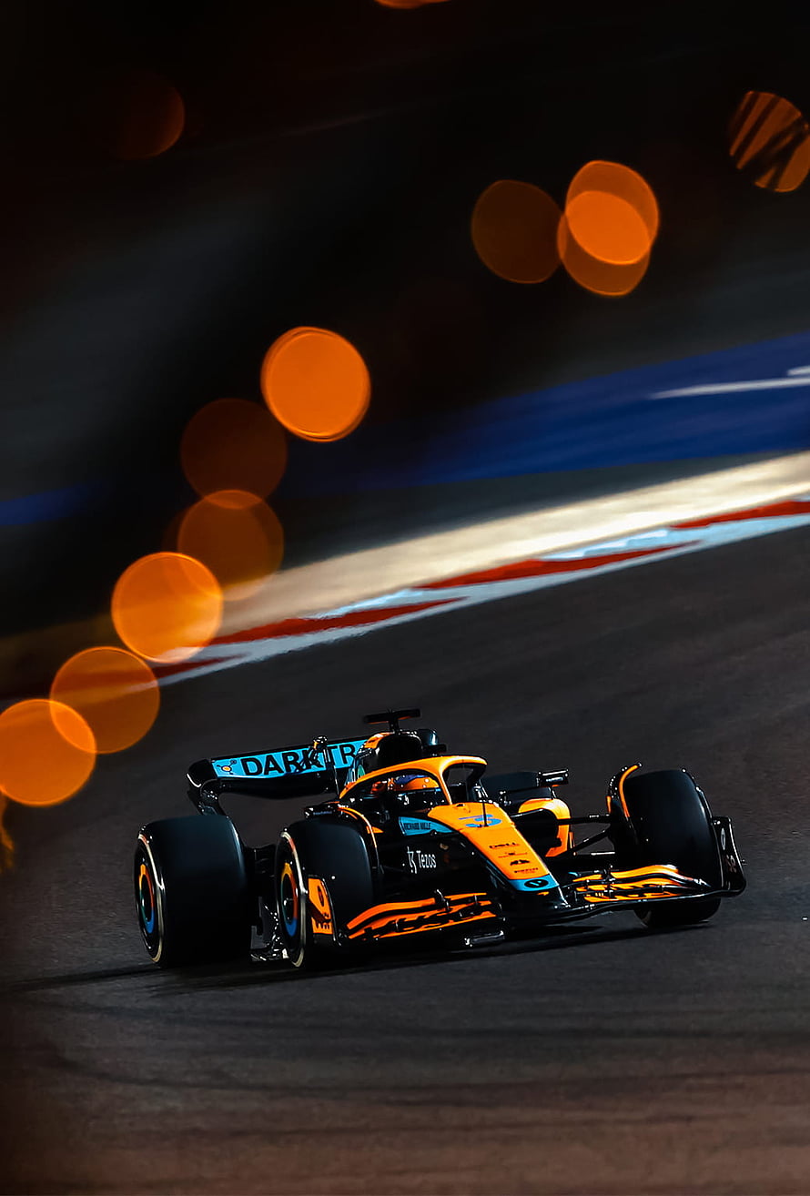 McLaren Formula 1 race car speeding on a night circuit with glowing orange bokeh lights HD phone wallpaper