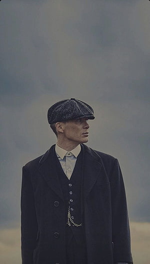 Thomas Shelby from Peaky Blinders wearing flat cap and dark coat against moody sky HD phone wallpaper