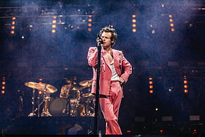 Harry Styles performing live on stage in a pink suit with dramatic concert lighting HD wallpaper
