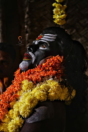 Swami Koragajja Portrait with Black Face Paint and Vibrant Flower Garlands HD phone wallpaper