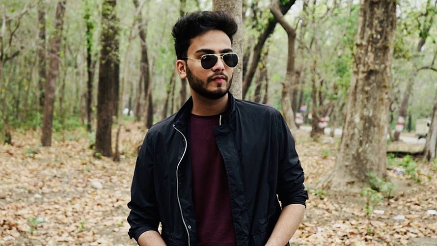 Elvish Yadav in a black bomber jacket and sunglasses standing in a forest HD wallpaper