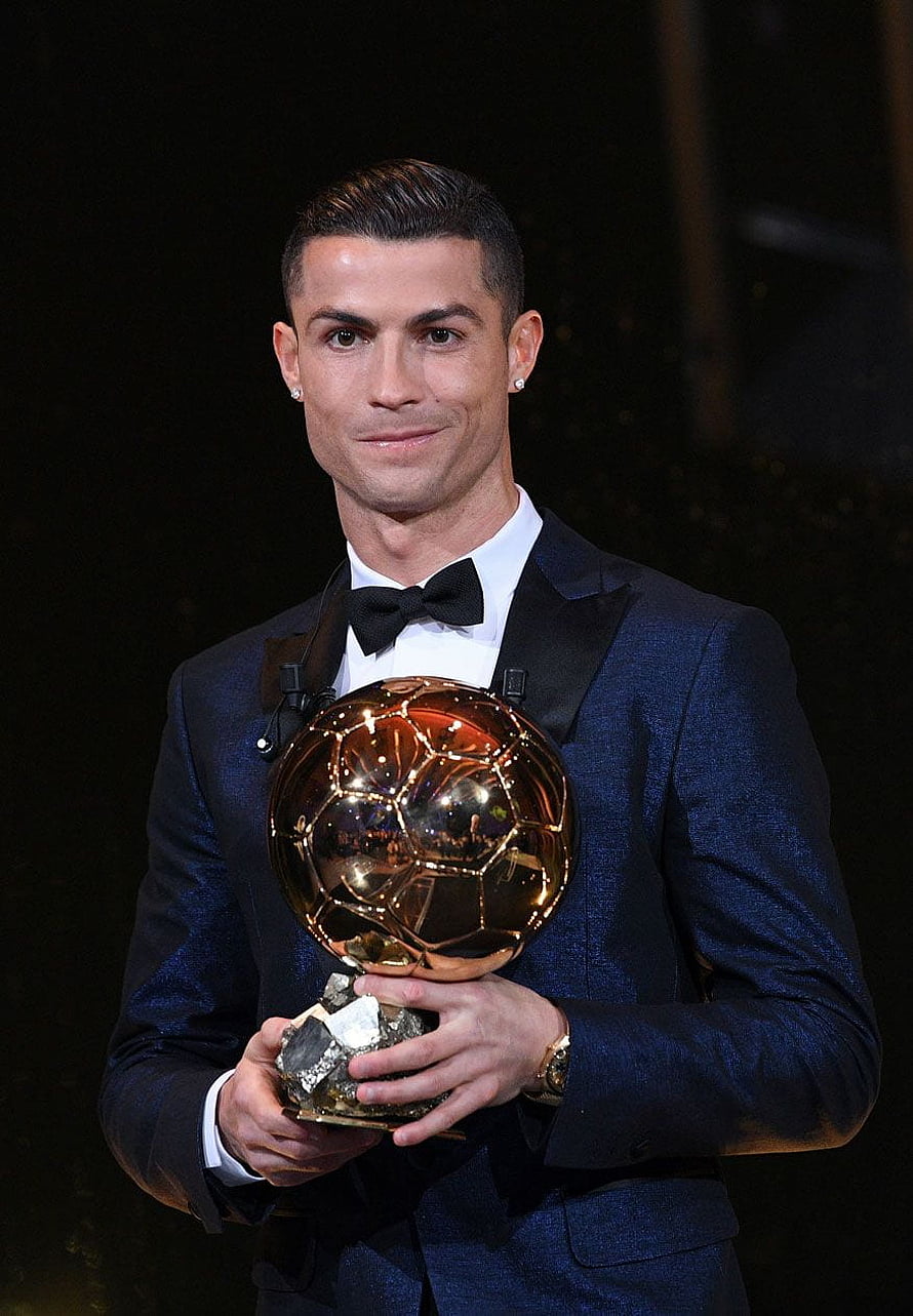 Cristiano Ronaldo in a navy tuxedo holding the golden Ballon d'Or trophy at an awards ceremony HD phone wallpaper