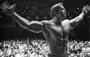 Arnold Schwarzenegger posing with arms raised at a bodybuilding competition in black and white HD wallpaper
