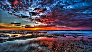 Dramatic Sunset Over Rocky Shoreline With Vibrant Clouds And Ocean Reflections HD wallpaper