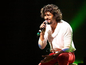 Sonu Nigam performing live on stage in a white shirt and red pants holding a microphone HD wallpaper