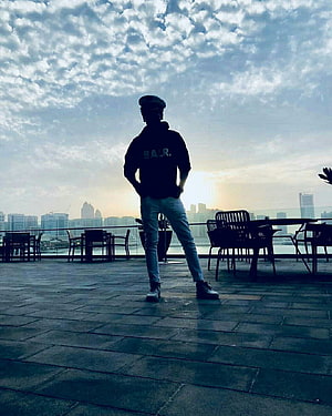 Silhouette of a man in a cap and hoodie standing on a rooftop terrace overlooking a city skyline at sunset, Whatsapp DP in 2021, instagram dp boys HD phone wallpaper
