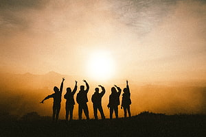 Silhouetted friends celebrating together on a mountain ridge at golden hour sunset HD wallpaper