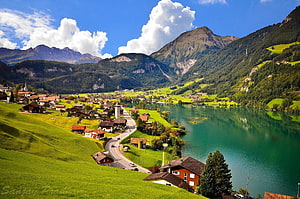 Scenic View of a Swiss Village by a Turquoise Lake Surrounded by Green Hills and Mountains HD wallpaper