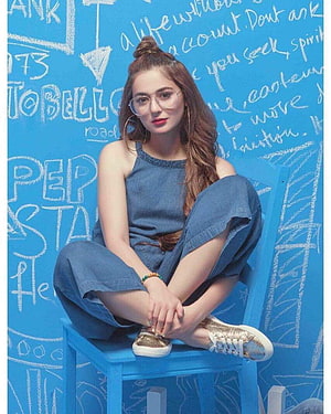 Hania Amir Sitting on a Blue Chair Against a Chalkboard Wall Wearing Denim Outfit HD phone wallpaper