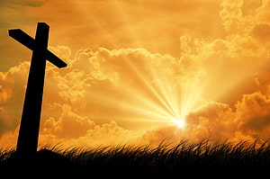 Silhouette of a Christian cross against a golden sunset sky with radiant sunburst and dramatic clouds HD wallpaper