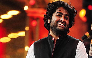 Arijit Singh smiling in a black vest and white shirt against a warm bokeh background HD wallpaper