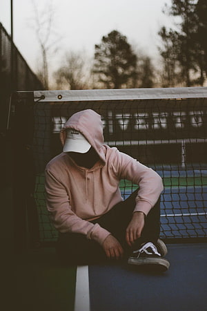 Person in Pink Hoodie and White Cap Sitting on Tennis Court HD phone wallpaper