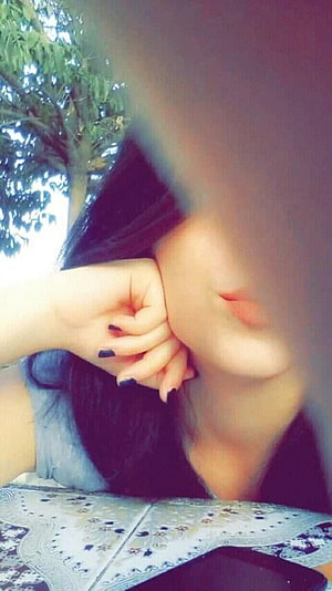 Close-up portrait of a girl with dark hair resting her chin on her hand, featuring black nail polish and a blurred face, set against a background of green trees and a patterned tablecloth. HD phone wallpaper