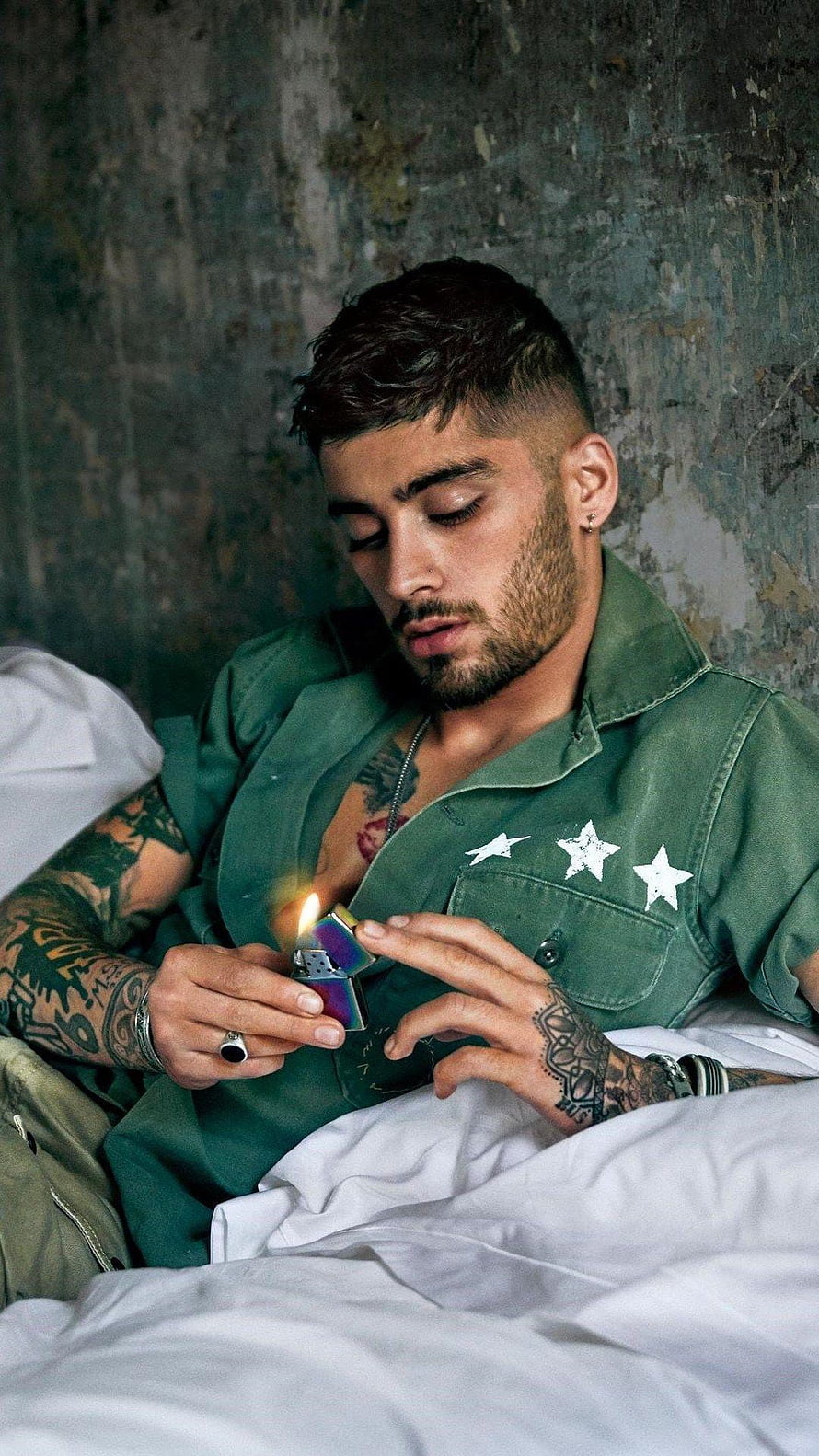 Zayn Malik in Green Star Shirt Holding a Lit Lighter Against a Textured Wall HD phone wallpaper
