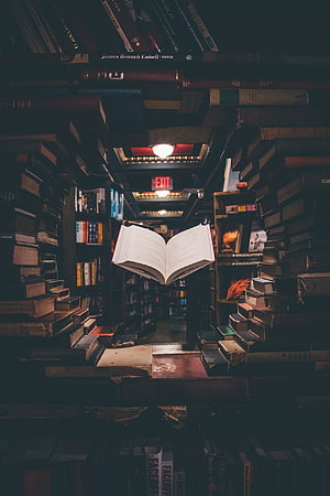 Open Book Floating in a Dark Library Aisle Surrounded by Stacked Volumes HD phone wallpaper