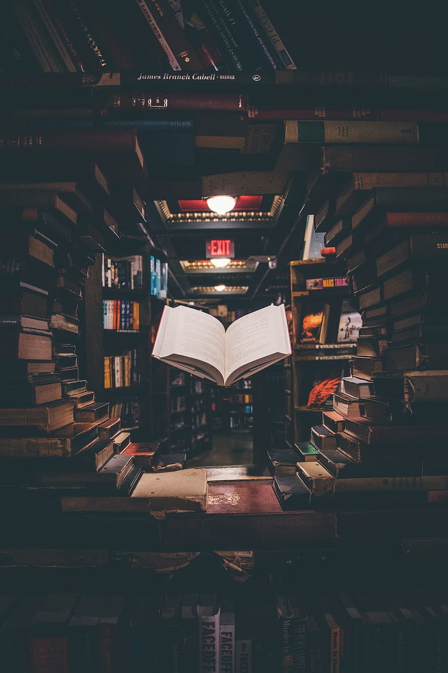 Open Book Floating in a Dark Library Aisle Surrounded by Stacked Volumes HD phone wallpaper