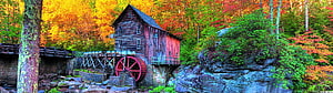 Historic wooden grist mill with red water wheel surrounded by vibrant autumn foliage and rocky terrain HD wallpaper