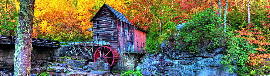 Historic wooden grist mill with red water wheel surrounded by vibrant autumn foliage and rocky terrain HD wallpaper