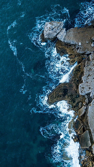 Aerial View of Turquoise Ocean Waves Crashing Against Rocky Coastline HD phone wallpaper