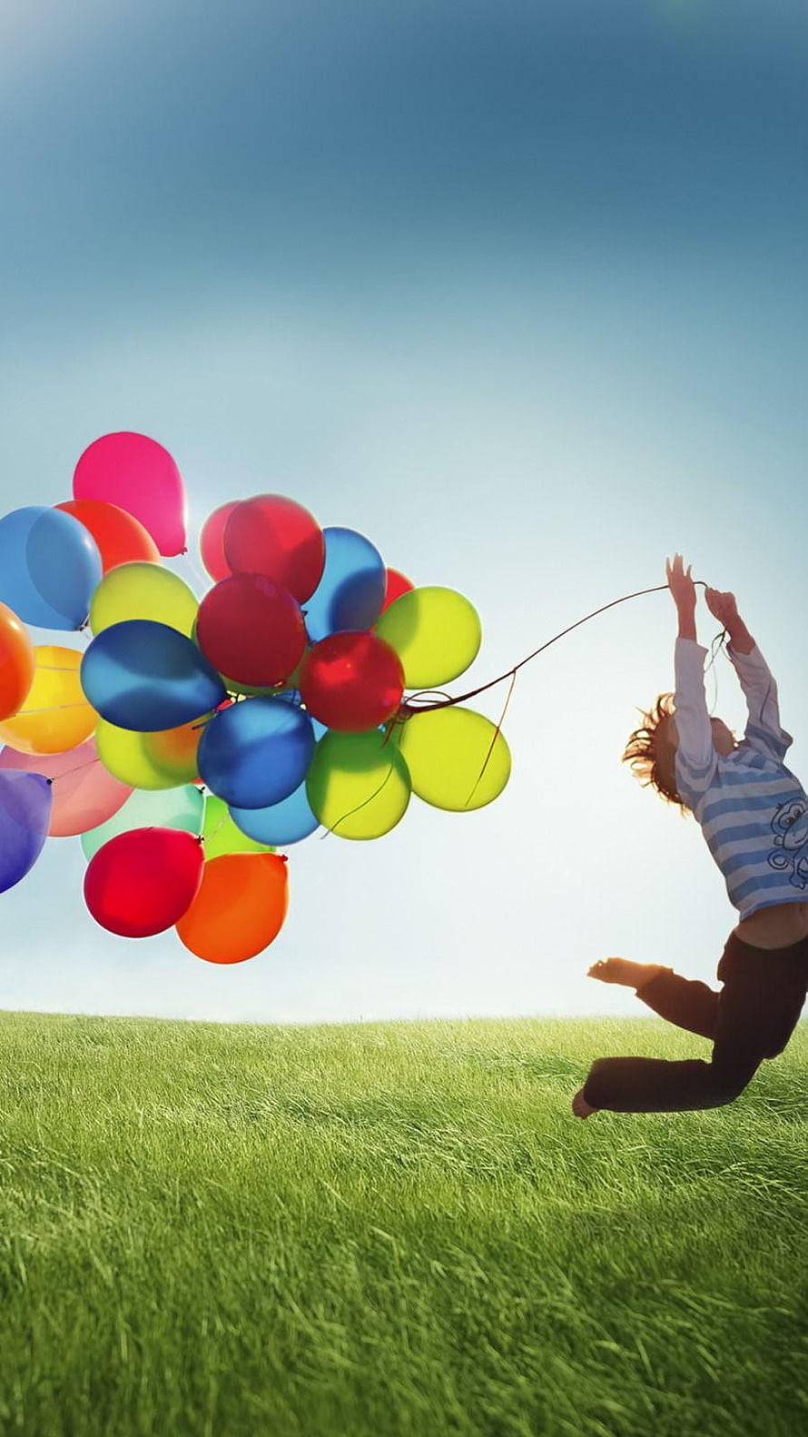 Child Leaping in Green Meadow Holding Vibrant Rainbow Balloons Against Clear Blue Sky HD phone wallpaper