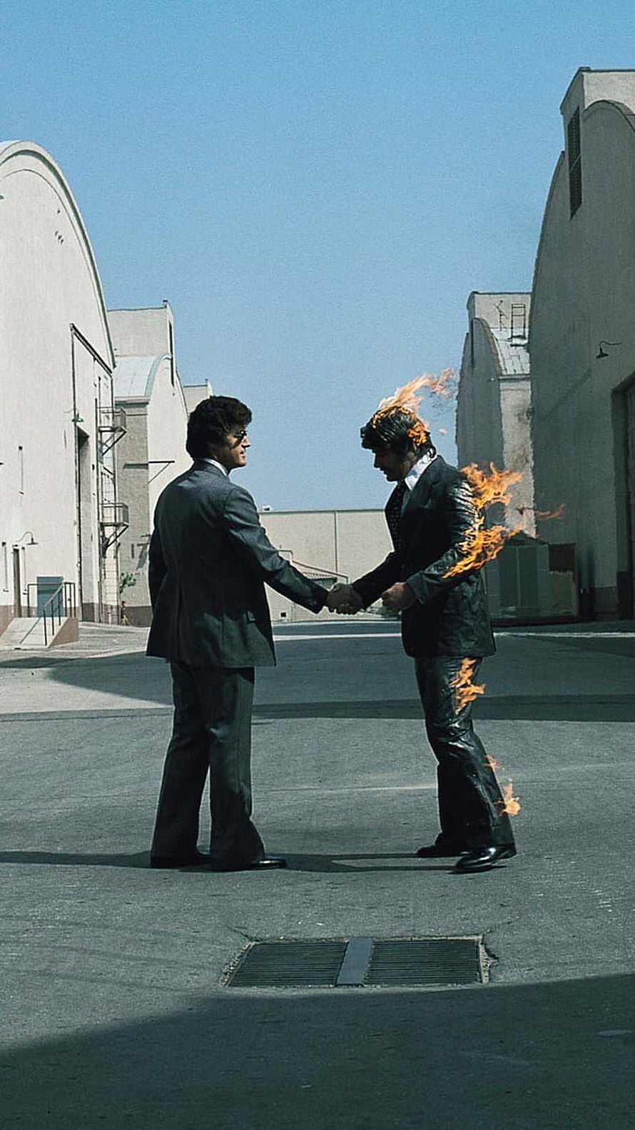 Two men in suits shaking hands in an industrial courtyard while one is engulfed in flames HD phone wallpaper
