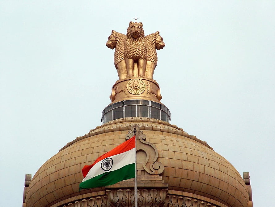 Golden Lion Capital of Ashoka atop the Indian Parliament House dome with the national flag waving against a clear sky HD wallpaper