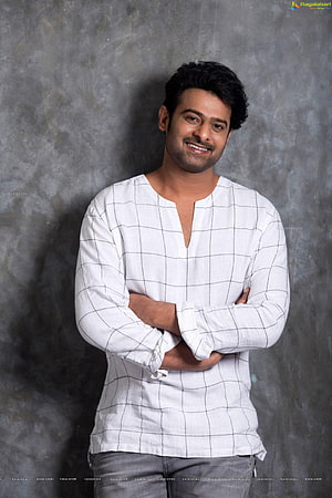 Prabhas in a white grid-patterned shirt with arms crossed against a textured grey studio backdrop HD phone wallpaper