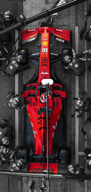 Top-down view of a red Ferrari Formula 1 car during a pit stop with mechanics working on tires HD phone wallpaper