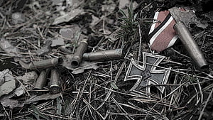 Abandoned Iron Cross Medal and Shell Casings in Overgrown Battlefield Debris HD wallpaper