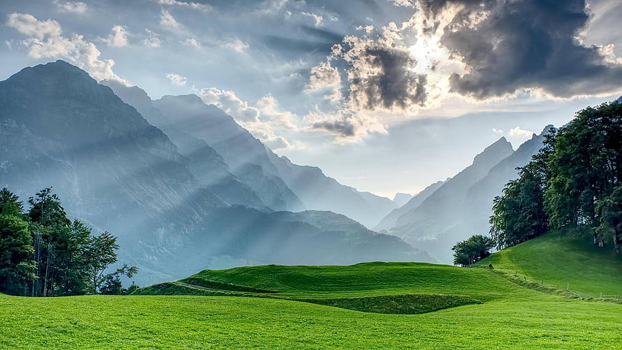 Sunbeams Over Green Pastures and Misty Peaks in Glarus Switzerland HD wallpaper