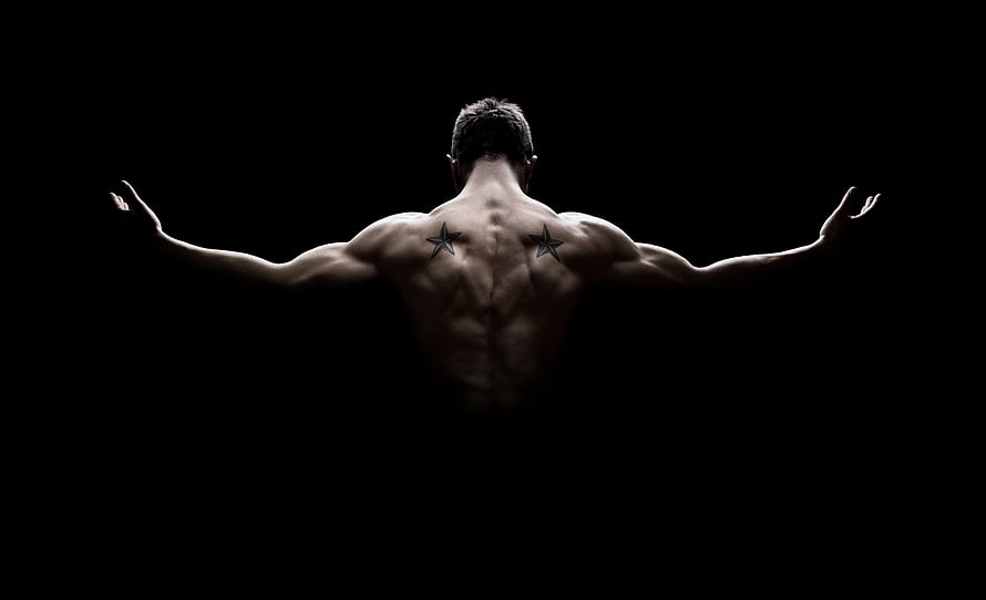 Muscular Male Back View with Star Tattoos and Arms Outstretched Against Black Background HD wallpaper