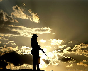 Silhouette of a soldier standing on a hilltop against a dramatic sunset sky with clouds HD wallpaper