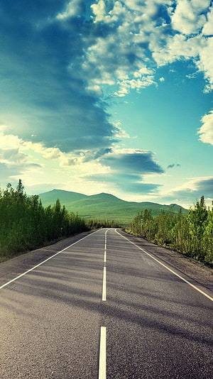 Endless asphalt highway stretching toward distant green mountains under a dramatic blue sky with fluffy clouds HD phone wallpaper