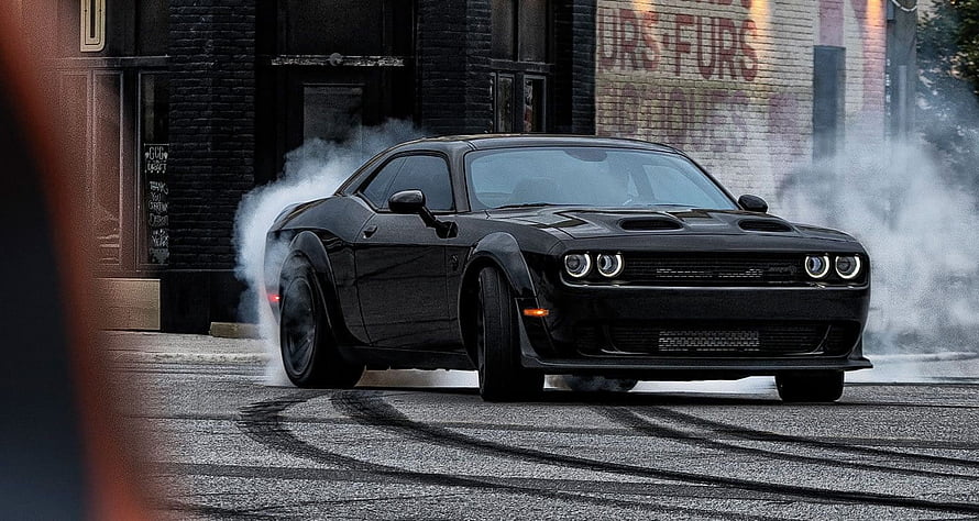Black Dodge Challenger SRT Demon performing a burnout on an urban street with tire smoke HD wallpaper