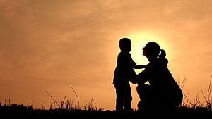 Silhouette of a mother and young son standing together in a field at sunset HD wallpaper