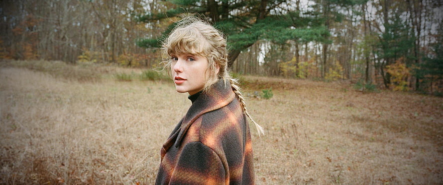 Taylor Swift in a plaid coat standing in an autumn field with a forest background HD wallpaper