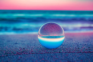 Crystal Clear Glass Sphere Reflecting Ocean Waves on Sandy Beach at Sunset HD wallpaper