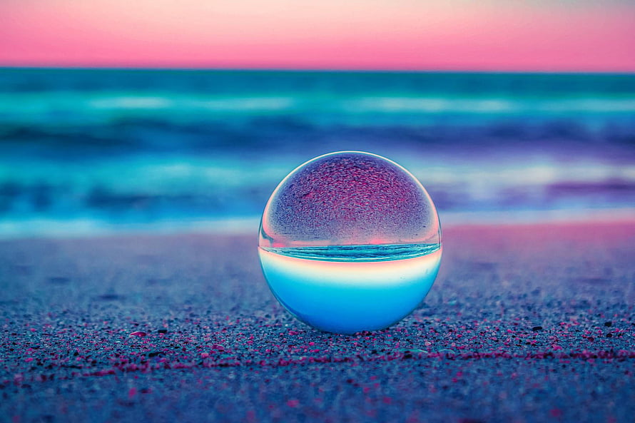 Crystal Clear Glass Sphere Reflecting Ocean Waves on Sandy Beach at Sunset HD wallpaper