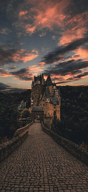 Eltz Castle in Germany at Sunset with Dramatic Orange Clouds and Cobblestone Bridge, nature, harry potter mobile HD phone wallpaper