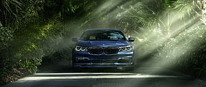 Blue BMW 7 Series Sedan Parked on a Sunlit Tropical Road HD wallpaper