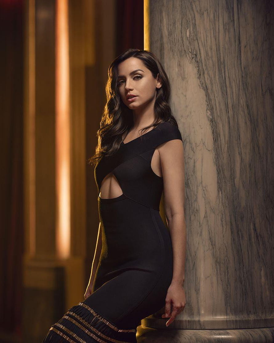 Ana de Armas in a black cutout dress leaning against a marble column with warm golden lighting HD phone wallpaper