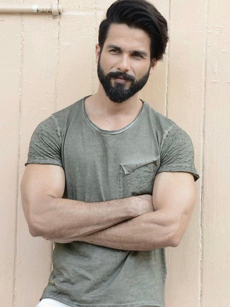 Shahid Kapoor in a casual olive t-shirt with a full beard, arms crossed against a textured wall HD phone wallpaper
